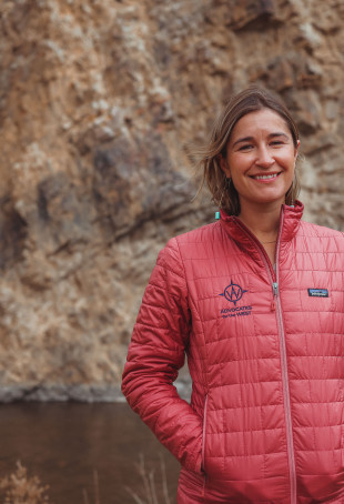 Hannah smiling outside near water, wearing a red puffer jacket.