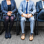 A variety of applicants are sitting in chairs, ready and waiting to interview.