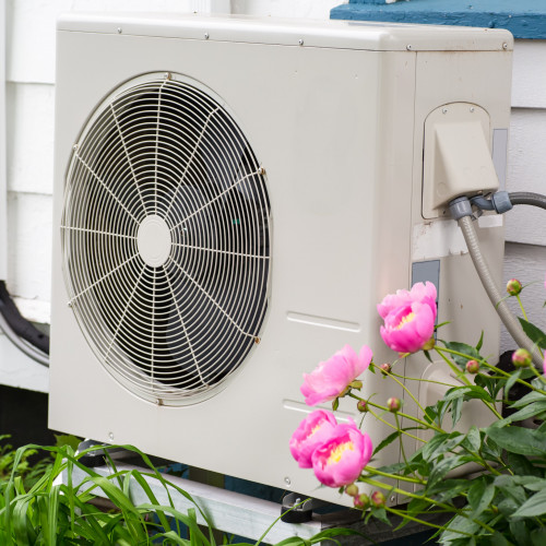 Air conditioning/ Heat pump unit on the side of a home among the flowers.