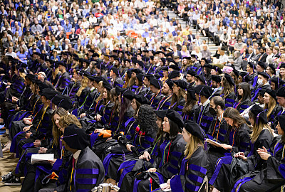 Group of graduates in caps and gowns, seated in an auditorium.